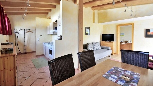A spacious living area with a wooden dining table, wicker chairs, a sofa, and a television. - Noichl's Hotel Garni  (Sankt Johann in Tirol)