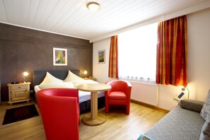 A modern hotel room with a bed, a round table, two red chairs, a grey sofa, and a window with curtains. - Noichl's Hotel Garni  (Sankt Johann in Tirol)