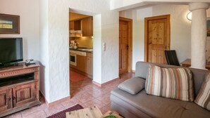 A living room with a sofa, a television, and a wooden cabinet. There is a kitchen visible through an open doorway. - Noichl's Hotel Garni  (Sankt Johann in Tirol)