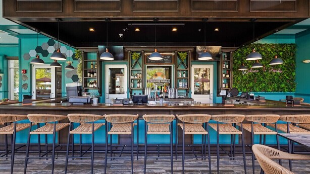 A bar area with a counter, bar stools, pendant lighting, and a green wall with a sign. - Blue Harbour Retreat: Private Pool, Free BBQ Grill (Davenport)