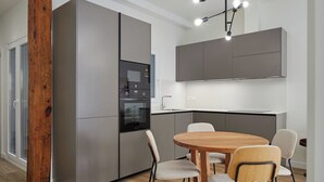 A modern kitchen with grey cabinetry, a built-in oven, and a dining area with a wooden table and chairs. - Kubo by FeelFree Rentals (San Sebastian)