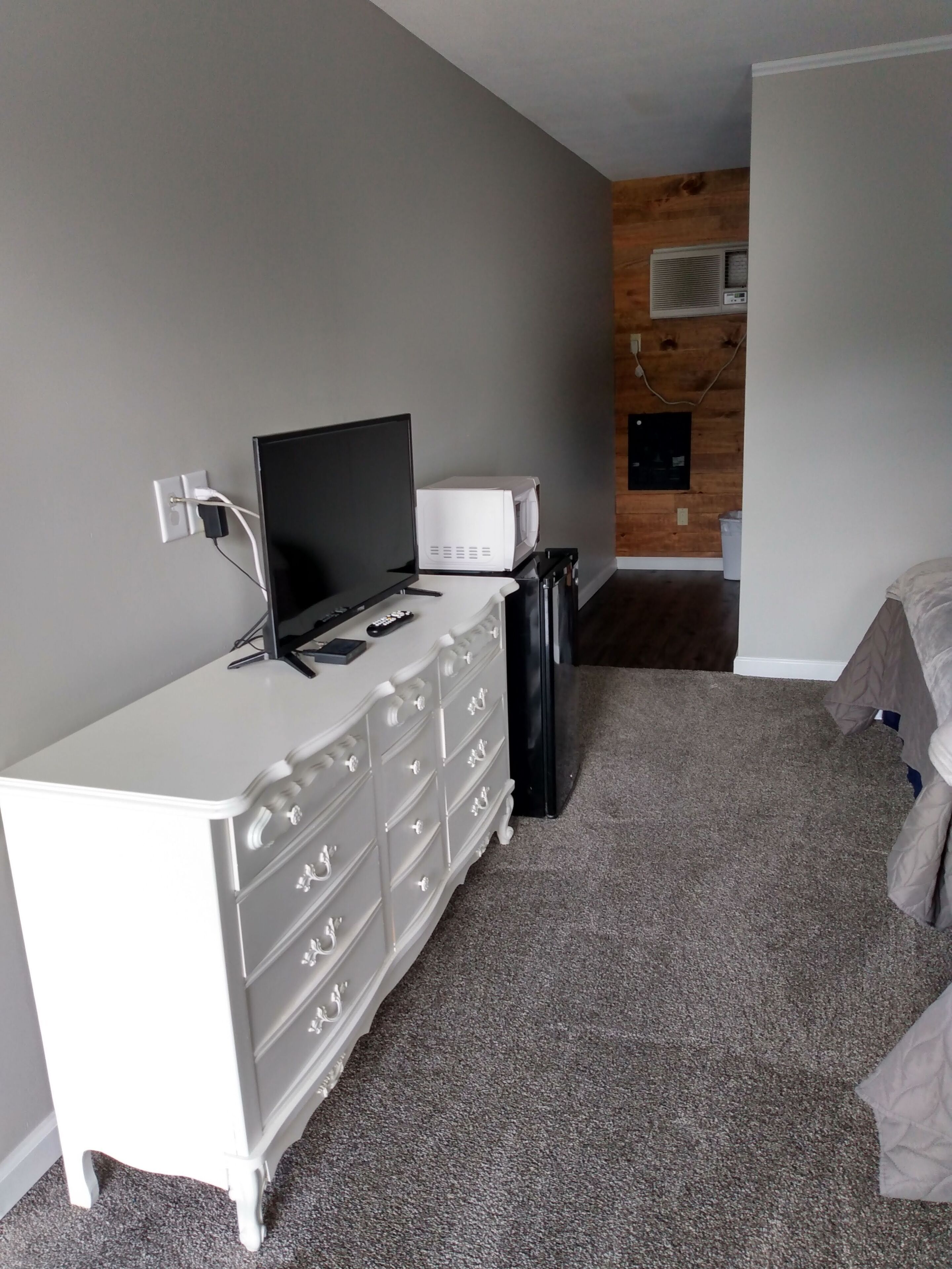 Une chambre avec une commode blanche, un téléviseur à écran plat, un four à micro-ondes et une poubelle.