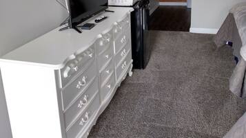 Une chambre avec une commode blanche, un téléviseur à écran plat, un four à micro-ondes et une poubelle.