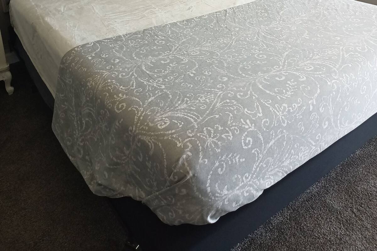 A neatly made bed with a patterned bedspread and pillows, a white headboard, and a window with curtains.
