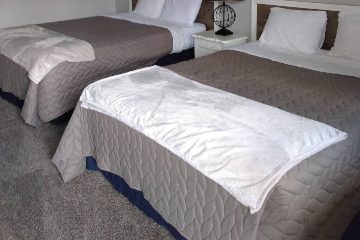 A hotel room with two beds, a nightstand with a lamp, and a painting on the wall.