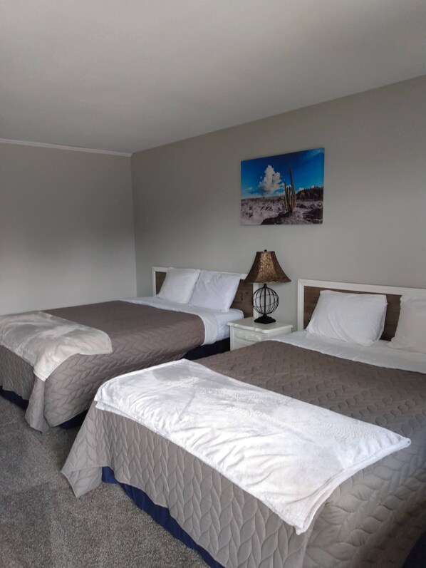 A hotel room with two beds, a nightstand with a lamp, and a painting on the wall.