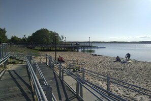 A pier extending into a calm body of water with a sandy beach and a metal walkway. - Holiday Home in Nowe Warpno by the Harbor (Nowe Warpno)
