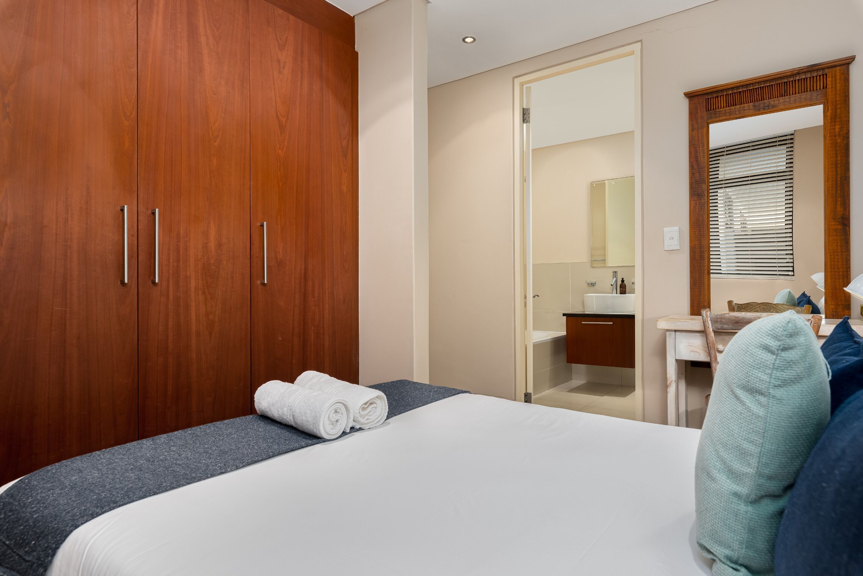Una camera d'albergo con un'ampia armatura in legno, un letto con lenzuola bianche, un bagno con lavandino e specchio, e una finestra con persiane.