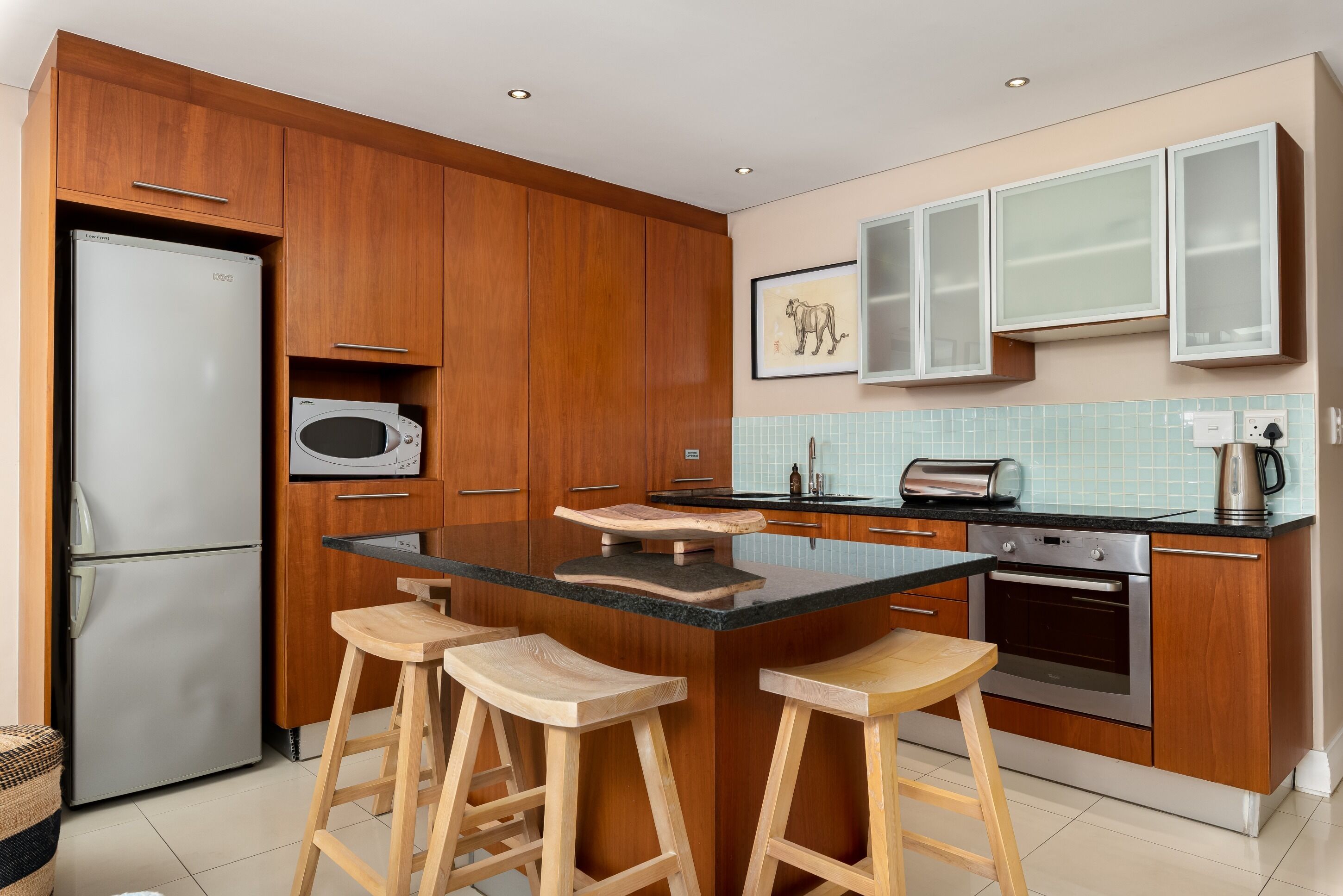 A modern kitchen with wooden cabinets, a built-in microwave, a toaster, and a large island with stools.