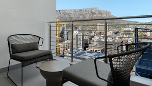 En balkon med to stole og et lille bord, udsigt over bybilledet med bygninger og et markant bjerg i baggrunden.