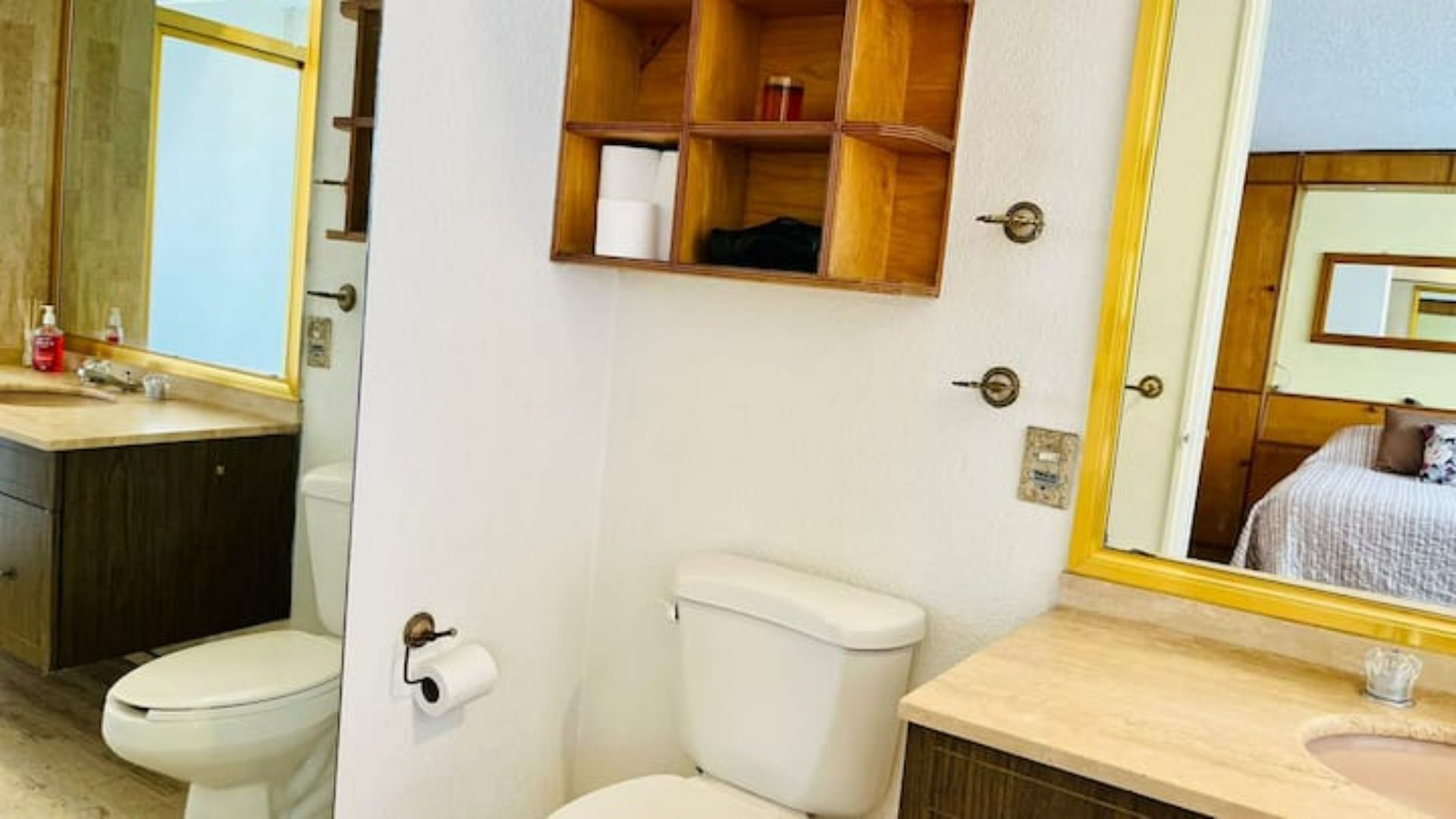 Et badeværelse med toilet, vask, spejl og et hyldesæt med toiletartikler.