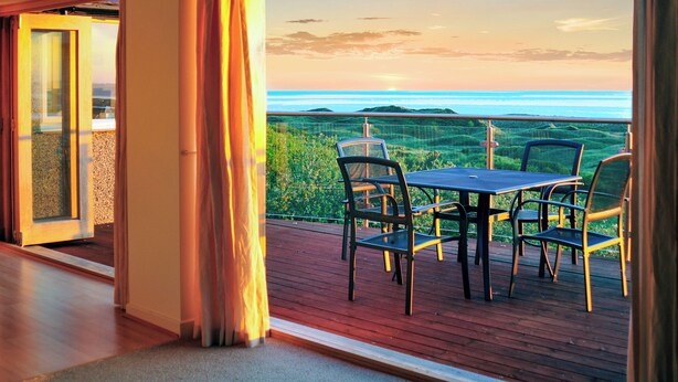 Un balcon avec une table et des chaises, donnant sur un paysage pittoresque composé de collines et d’une étendue d’eau.