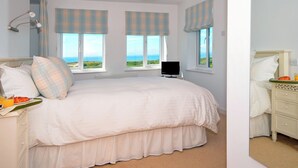 Une chambre à coucher avec un lit, une table de chevet, une télévision et des fenêtres donnant sur la mer.