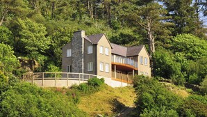 Une maison à deux étages avec une façade en pierre, un balcon et une vue sur une colline boisée.