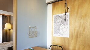 A hotel room with a wooden table, two chairs, a map of Tokyo on the wall, and a lamp.
