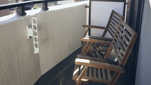 A balcony with a wooden chair and a whiteboard, overlooking a cityscape with high-rise buildings.