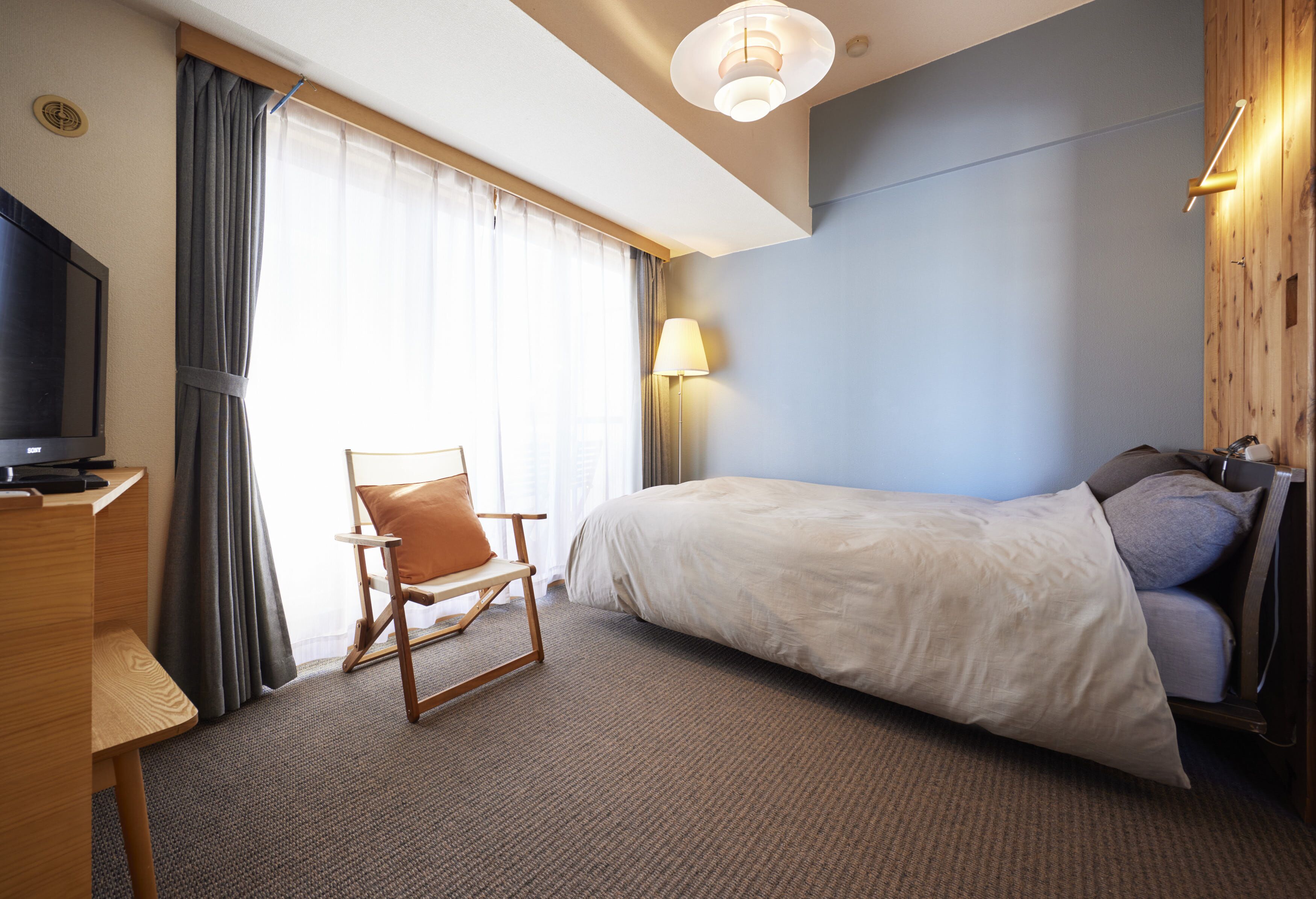 Une chambre d’hôtel équipée d’un lit, d’un bureau, d’une chaise, d’une télévision et d’une fenêtre avec des rideaux.