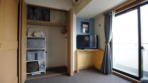 A room with a wardrobe, a TV, and a large window with curtains.