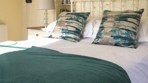 A neatly made bed with a green blanket and two patterned pillows, a bedside table with a lamp, and a bookshelf in the background. - 2 bedroom accommodation in Madron, near Penzance (Madron, near Penzance)