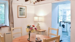 A dining area with a wooden table, chairs, a vase with flowers, a lamp, and a framed picture on the wall. - 2 bedroom accommodation in Madron, near Penzance (Madron, near Penzance)