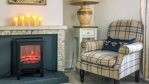 A cozy room with a fireplace, a plaid armchair, a lamp, and candles. - 2 bedroom accommodation in Madron, near Penzance (Madron, near Penzance)