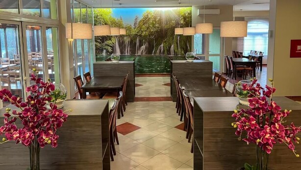 A modern dining area with a central waterfall feature, surrounded by tables and chairs. - Hotel Babic (Plitvicka Jezera)