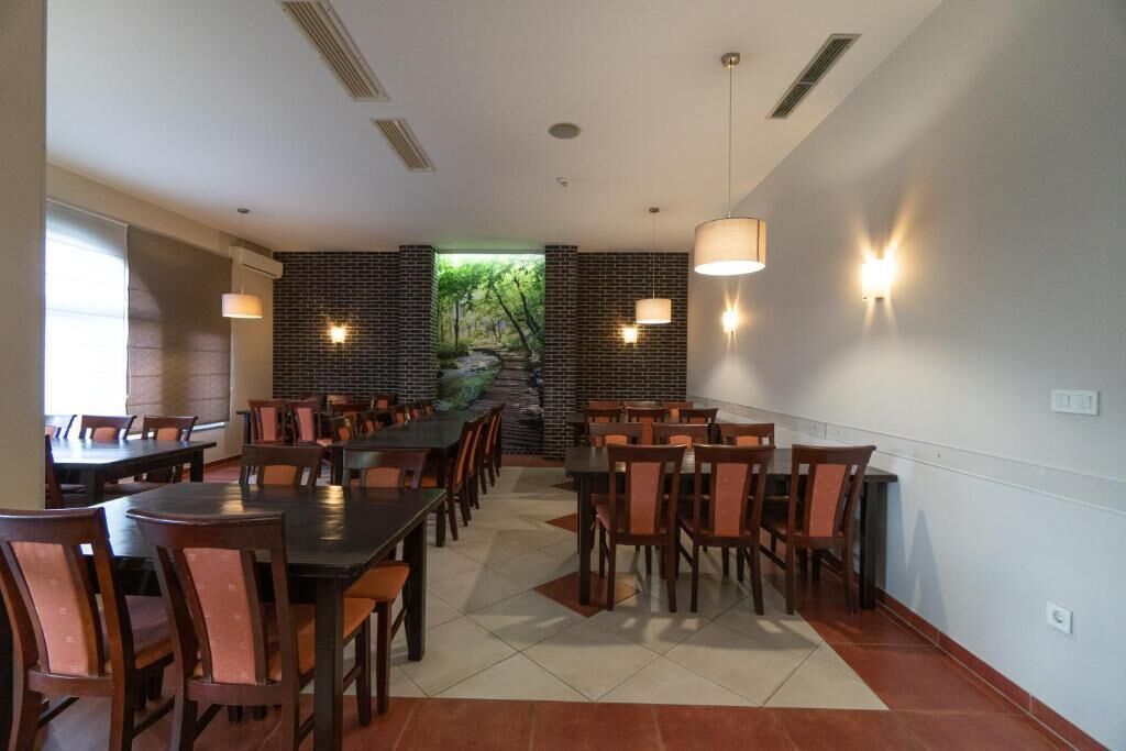 Uma sala de jantar com várias mesas e cadeiras, uma parede de tijolos com um mural e iluminação pendente.