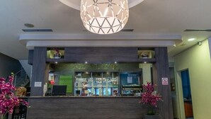 A modern reception area with a dark reception desk, a large geometric pendant light, and potted pink orchids. - Hotel Babic (Plitvicka Jezera)