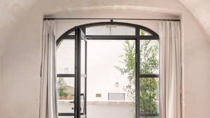 Une chambre à coucher avec un lit, un banc et une grande fenêtre en arc surmontée de rideaux.