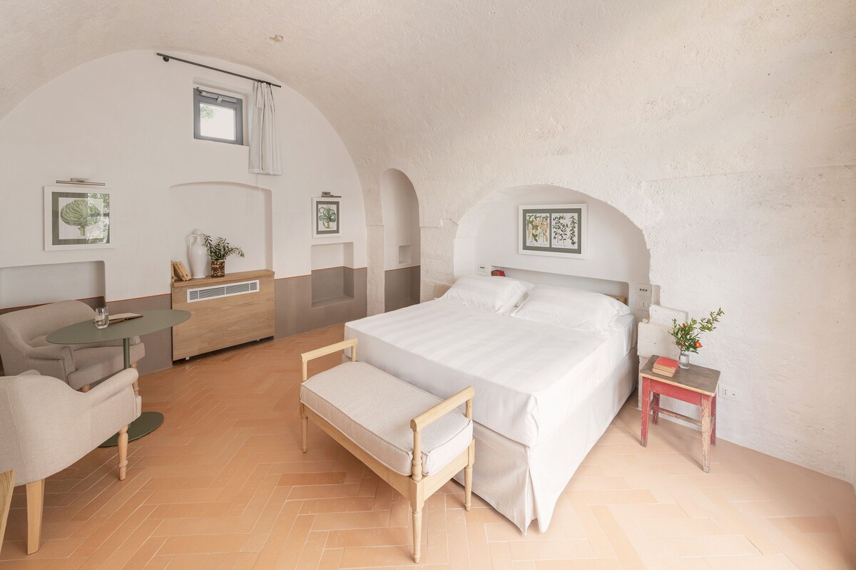 Um quarto com cama, mesa de cabeceira, cadeira, uma pequena mesa e um sofá.
