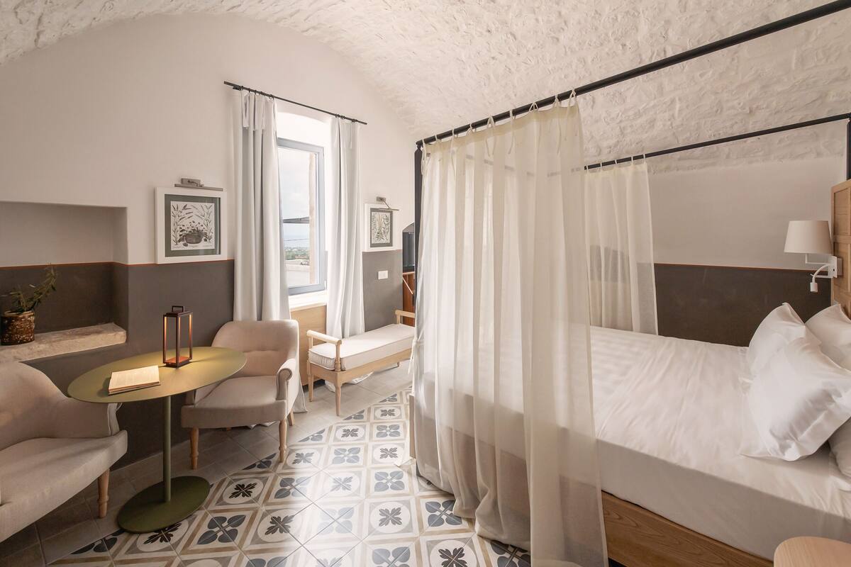 Quarto de hotel com uma cama, um sofá, uma mesinha e uma cadeira.