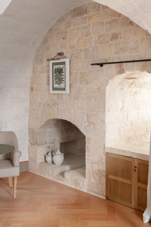Una habitación de paredes de piedra con chimenea, un grabado botánico enmarcado y un mueble de madera.