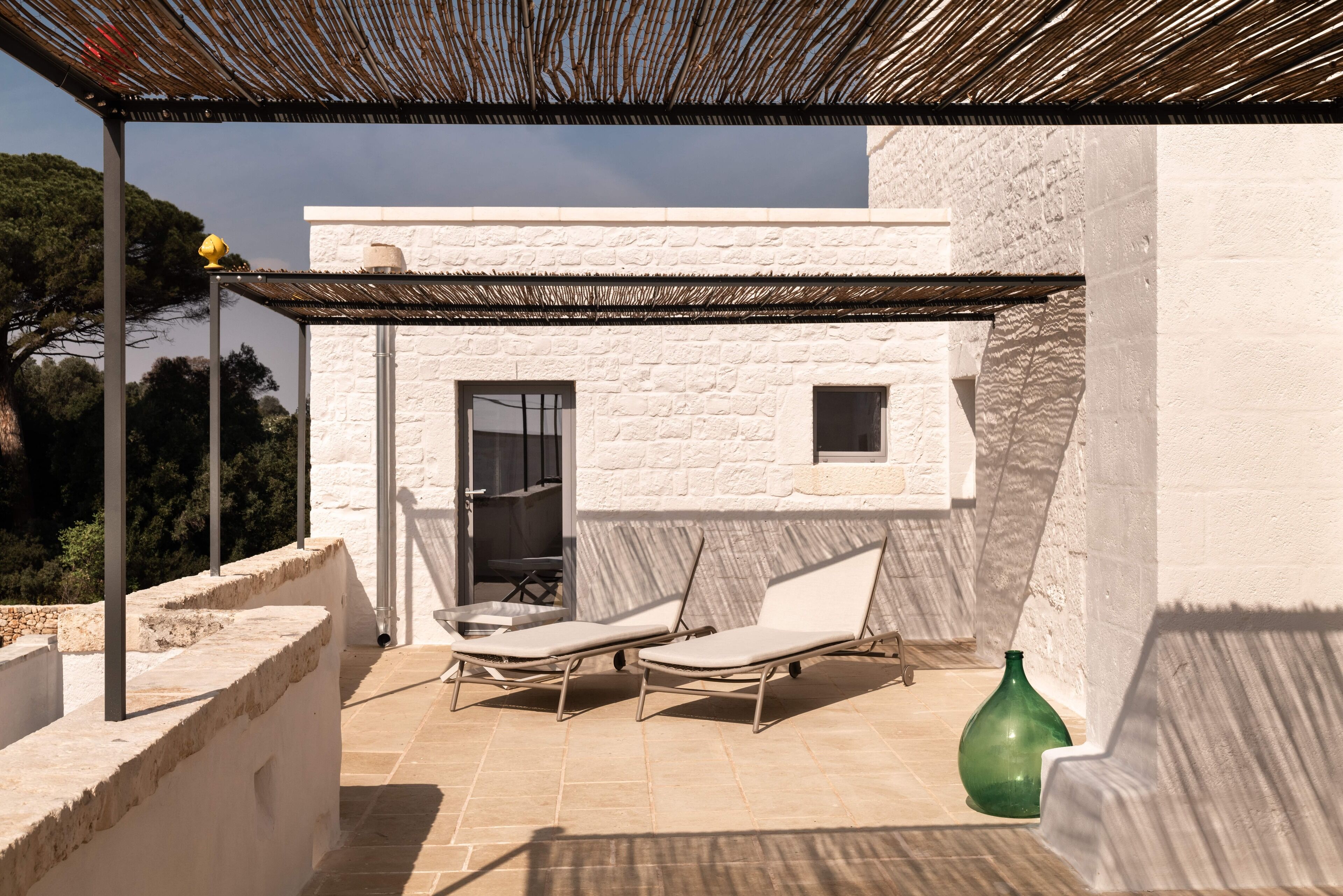 Una terraza con dos sillones de descanso, un jarrón verde y un edificio blanco de fachada de piedra.