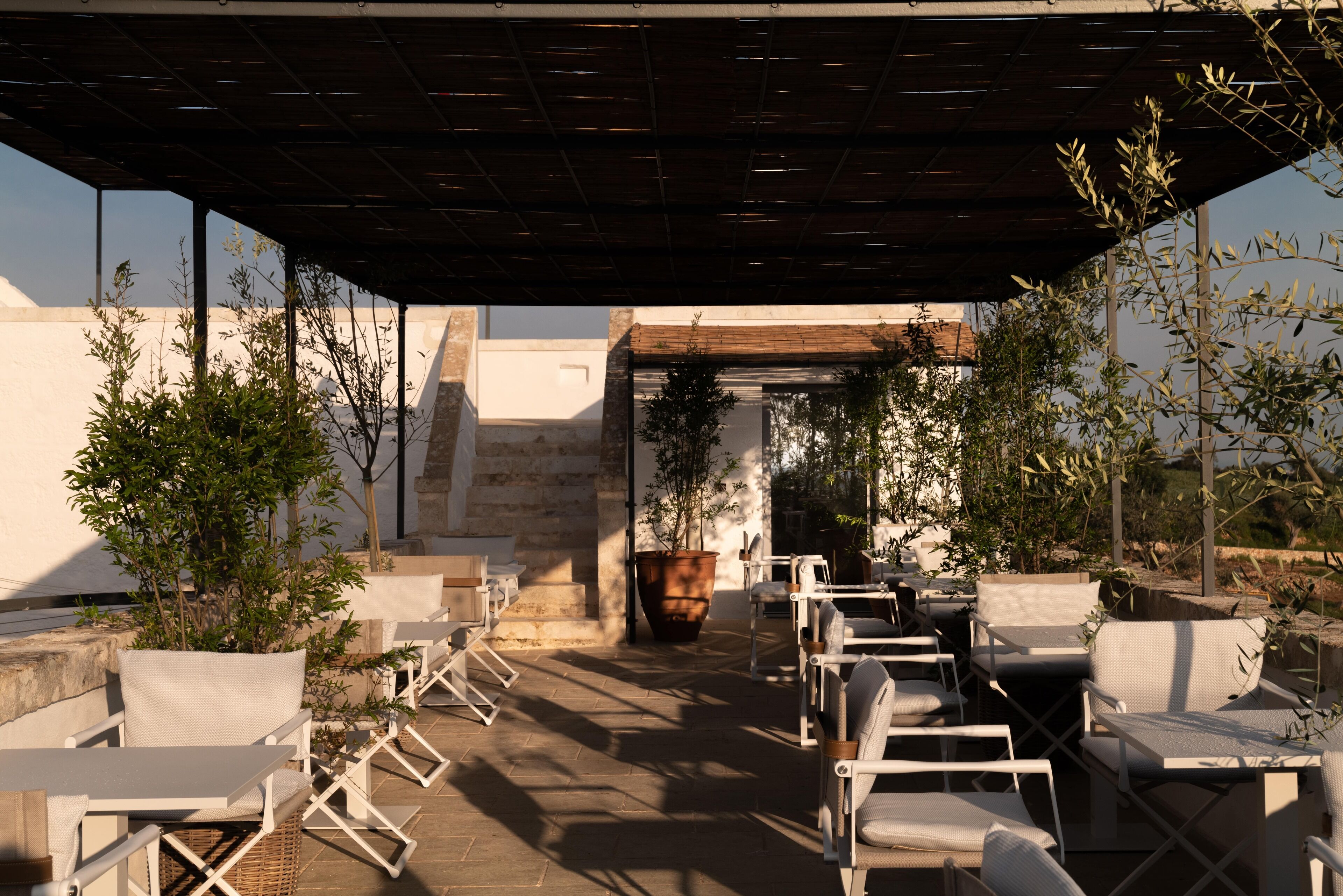 An outdoor patio with white furniture, a pergola, and potted plants.