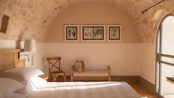 Un dormitorio con cama y silla de madera, un banco y reproducciones botánicas enmarcadas en la pared.