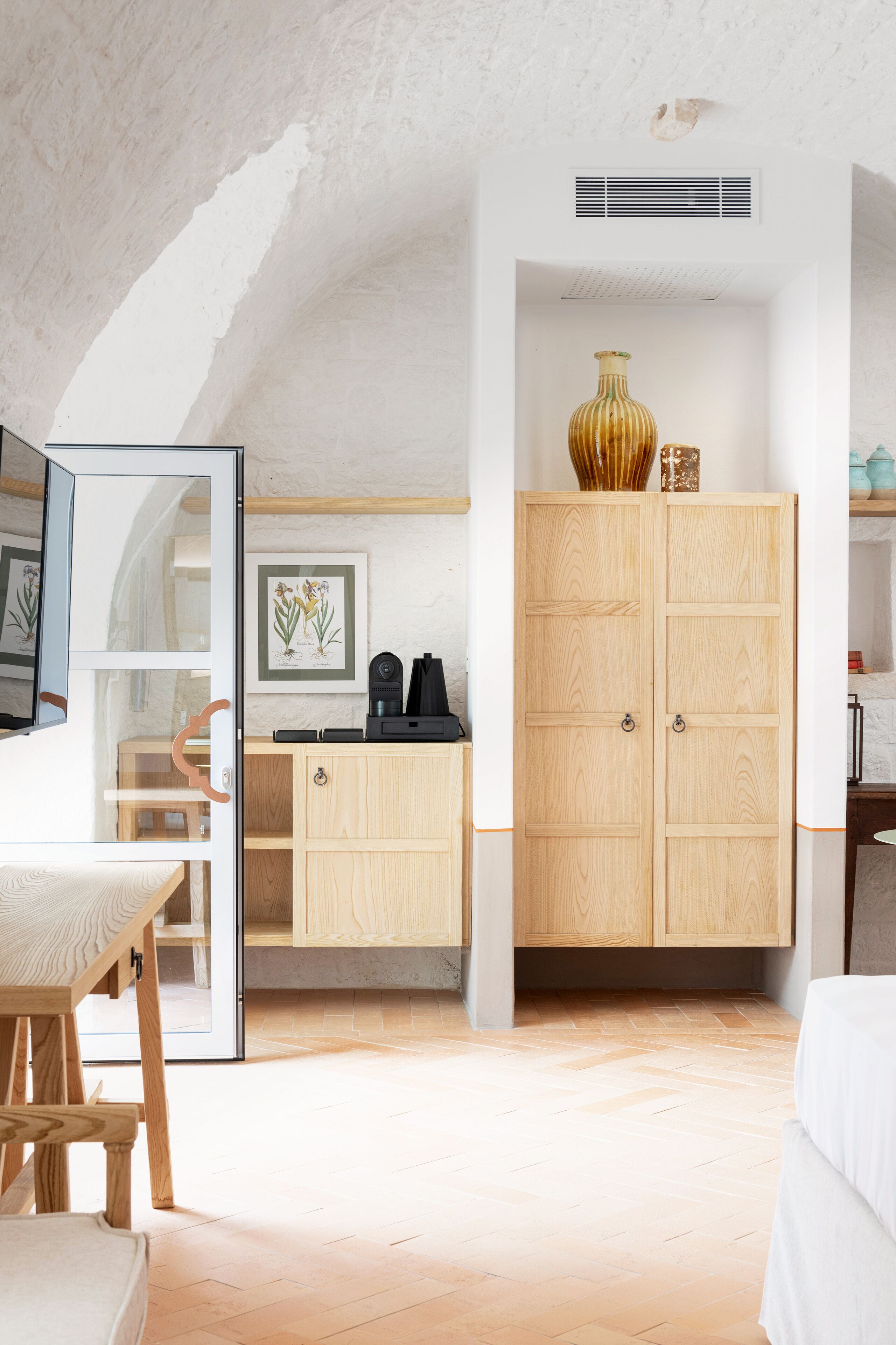 A room with a wooden cabinet, a framed botanical print on the wall, and a large vase on top of the cabinet.