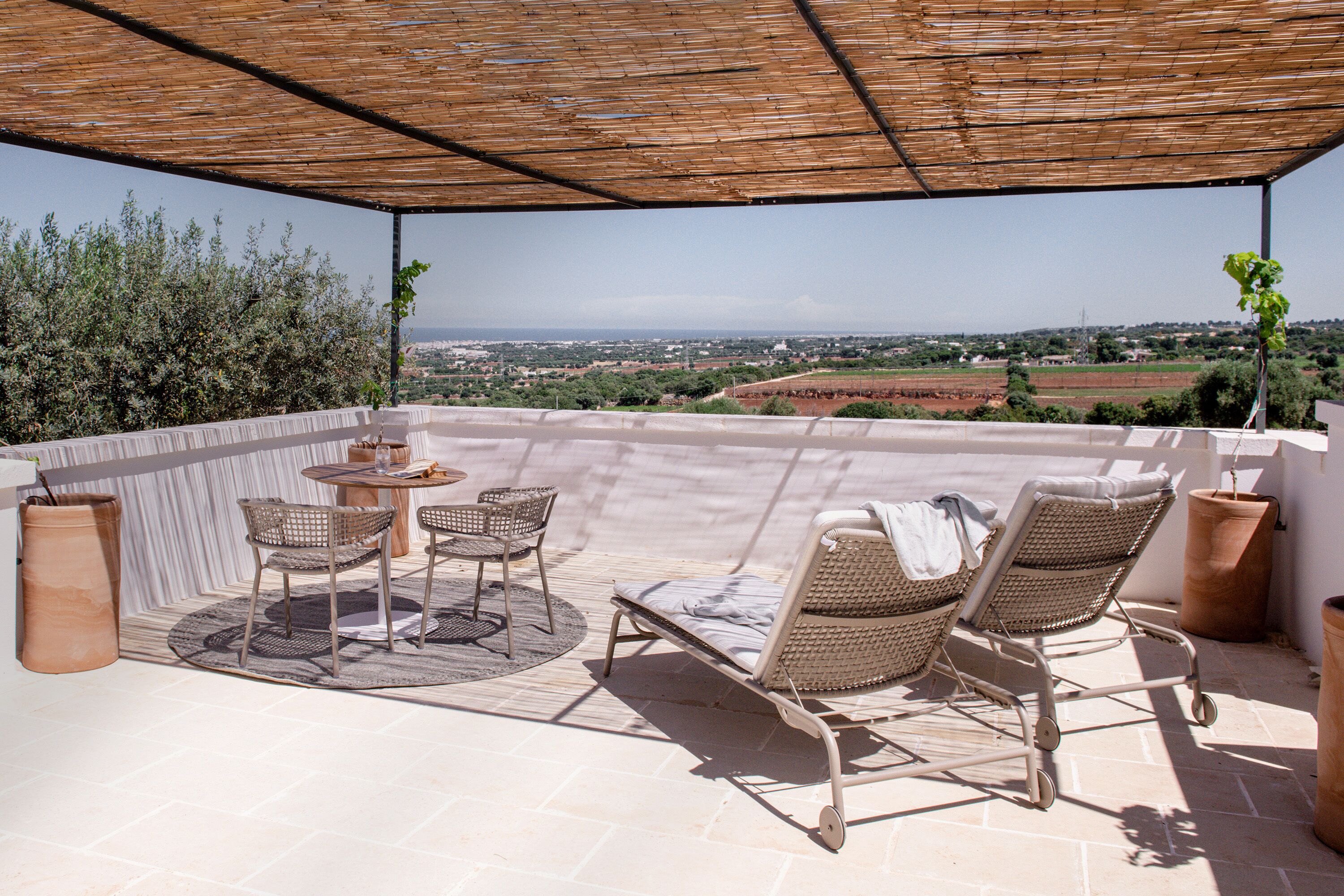 A covered outdoor seating area with wicker furniture, a small table, and a view of the countryside.