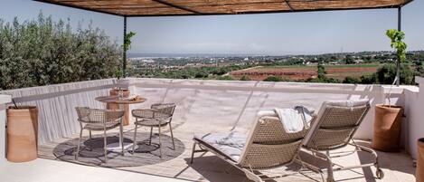 A covered outdoor seating area with wicker furniture, a small table, and a view of the countryside.