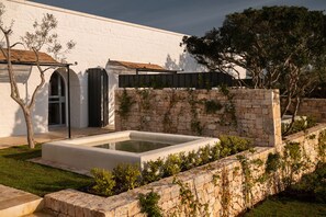 Un edificio moderno con fachada blanca, un muro de piedra y una piscina rectangular.