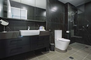 A modern bathroom with a dark marble sink, a toilet, and a glass-enclosed shower.