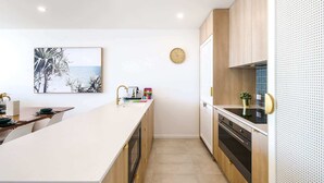 A modern kitchen with a long island counter, wooden cabinets, and a tiled backsplash. - Exquisite 1-Bed Apartment with Bay Views (Batemans Bay)
