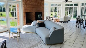 A spacious living room with a large gray sectional sofa, a fireplace, and a dining area with chairs and a table. - 6BR Waterfront Estate | Private Dock, Firepit, Screened Porch & Beach Access (Sherwood)