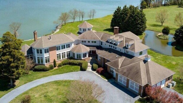 A large, multi-story house with a wrap-around porch, a circular tower, and a view of a lake. - 6BR Waterfront Estate | Private Dock, Firepit, Screened Porch & Beach Access (Sherwood)