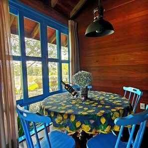 A round table with a floral tablecloth, surrounded by blue chairs, in a room with wooden walls and large windows.