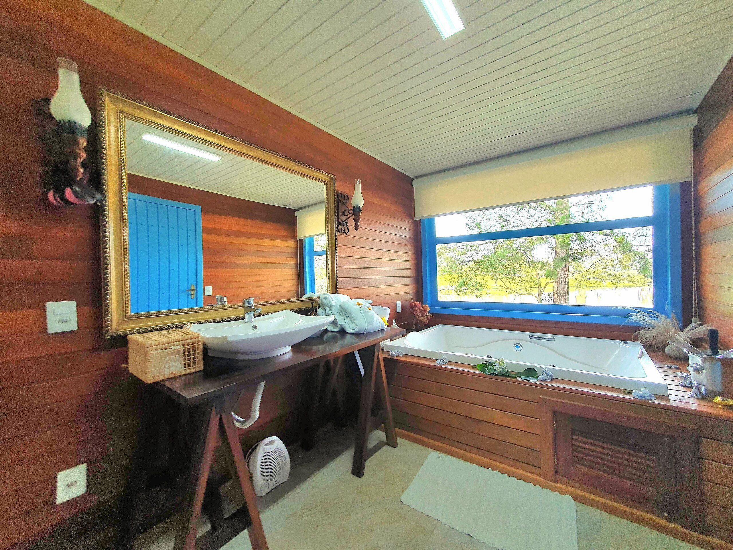 A bathroom with a large mirror, a sink, a bathtub, and a window with a view of trees.