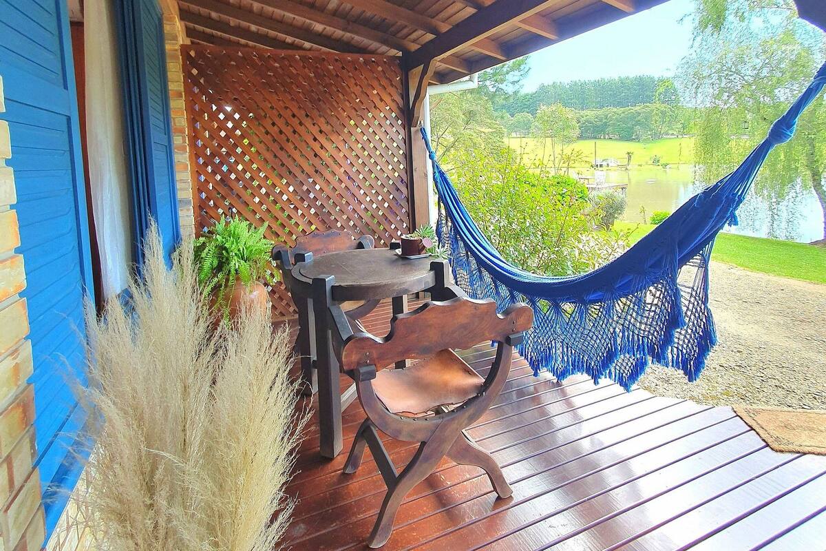 Un espace extérieur aménagé, abrité, avec une table et des chaises en bois, un hamac et une vue sur un paysage verdoyant.