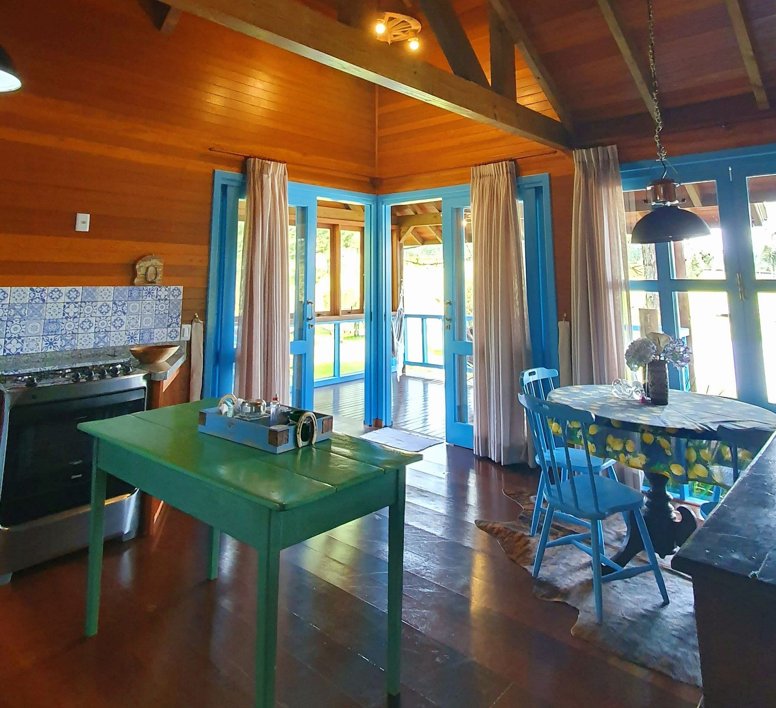 Une cuisine rustique avec des murs en bois, une table verte et des chaises bleues.