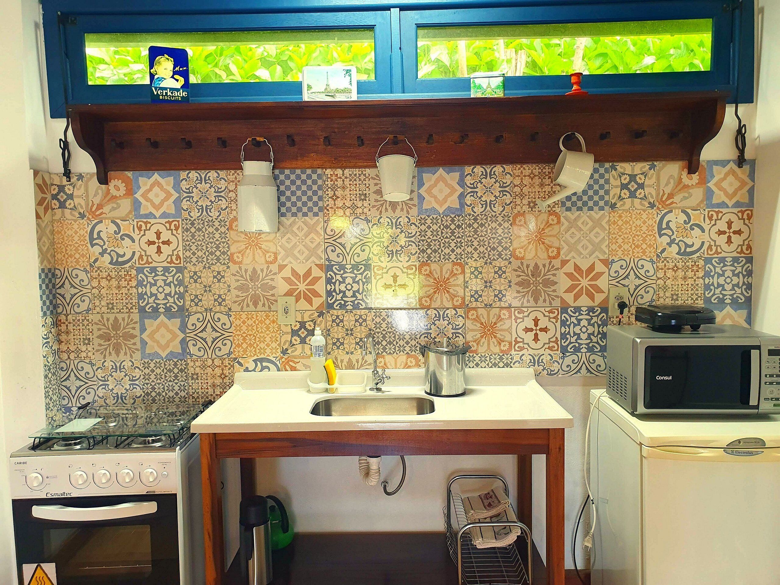 Een keuken met een gasfornuis, spoelbak en een magnetron. Boven de spoelbak is een raam met uitzicht op groen.