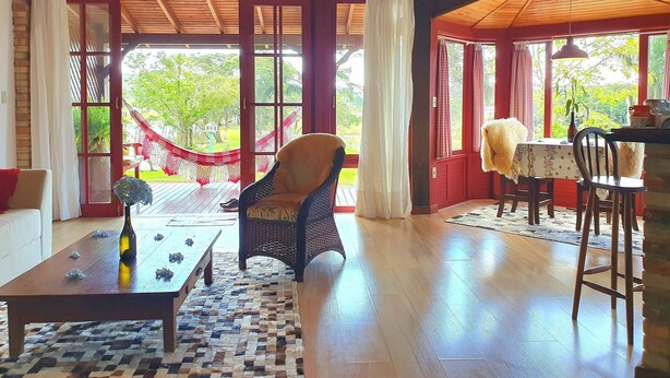 Une pièce chaleureuse avec un plafond en bois, un hamac, une table avec une bouteille, et une vue sur la verdure à l’extérieur.