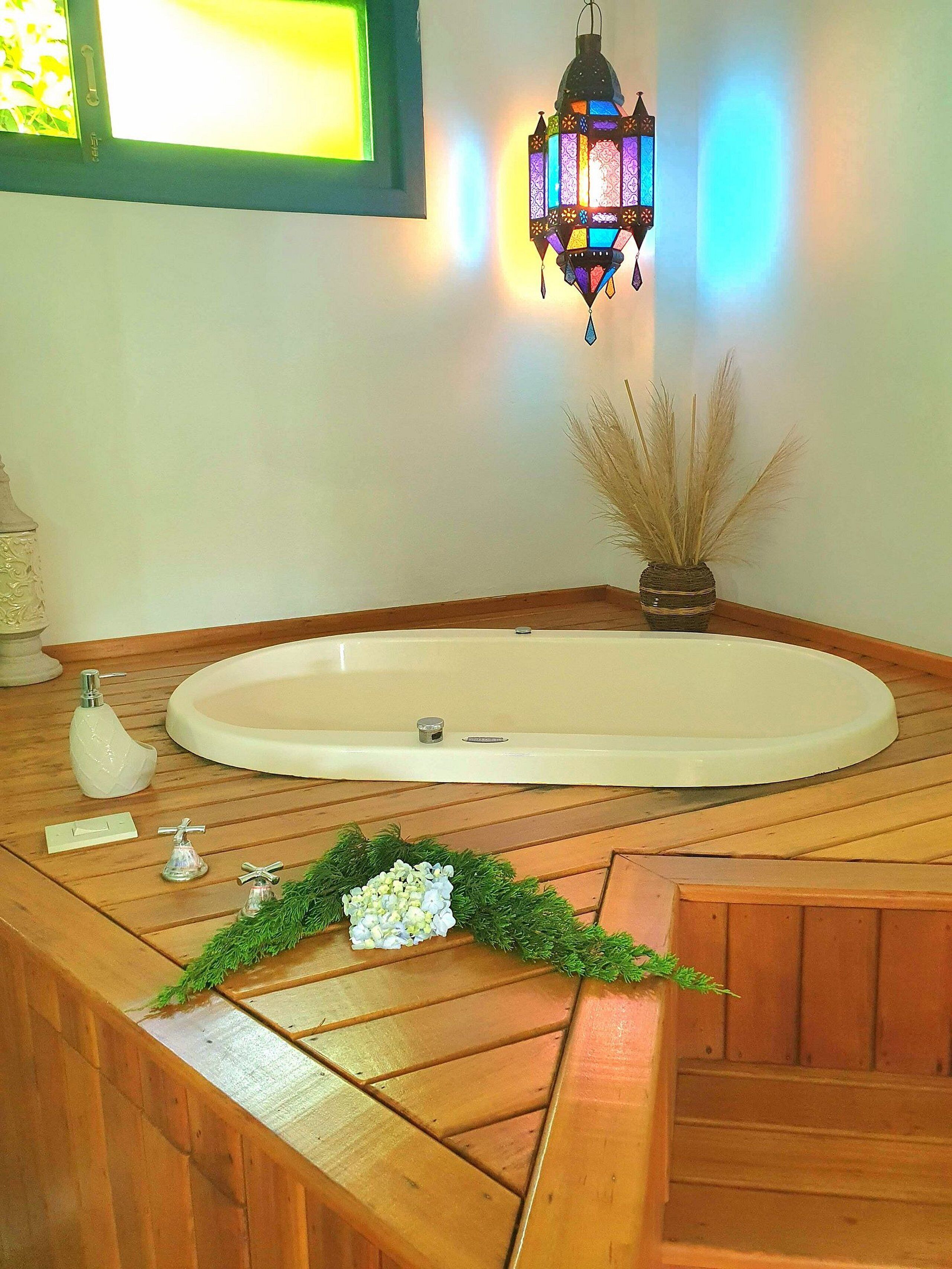 A bathroom with a wooden vanity, a white bathtub, a decorative lantern, and a window with a view of greenery.